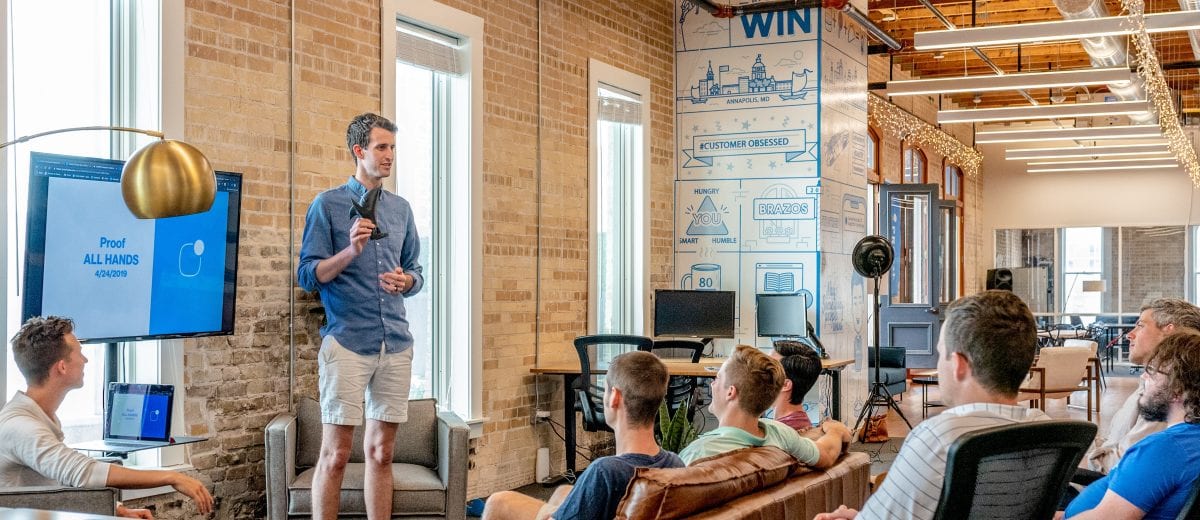 photo of man showing a presentation to a group of people siting in office lounge